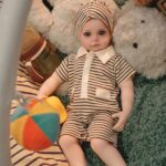 Silikonová panenka znovuzrozená s realistickými rysy, oblečená v pruhovaném oblečení, ležící na plyšové dece.