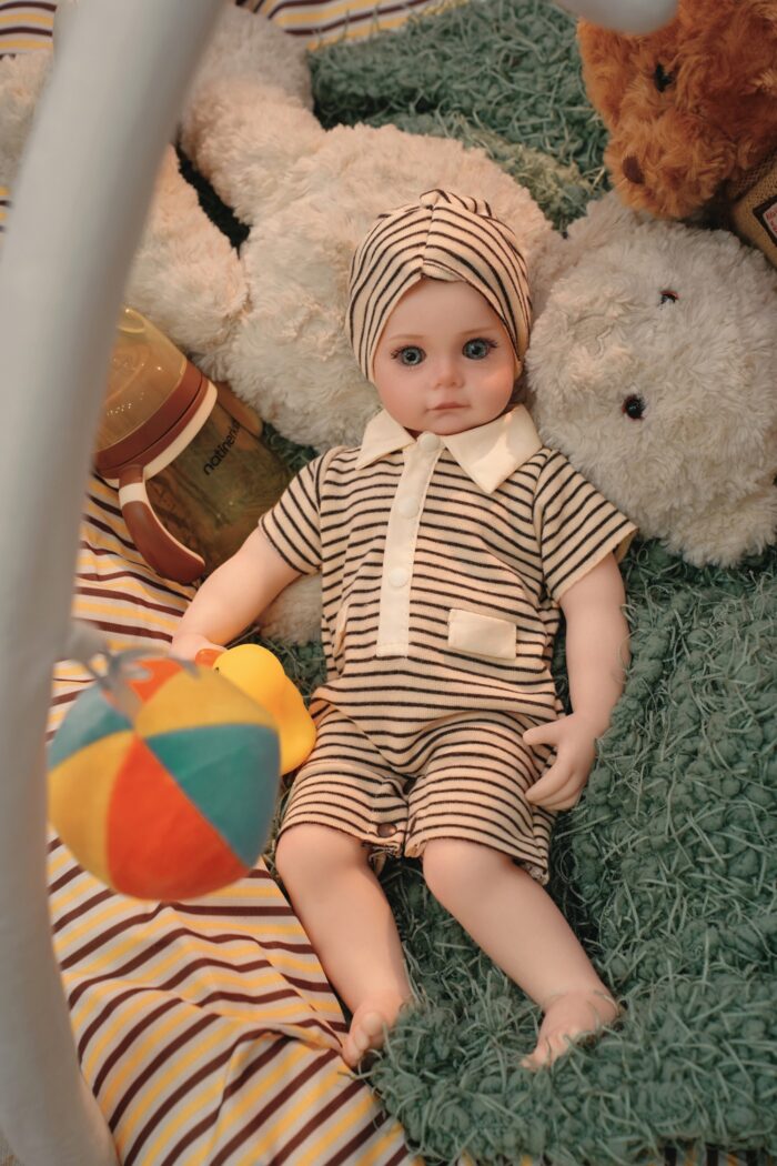 Silikonová panenka znovuzrozená s realistickými rysy, oblečená v pruhovaném oblečení, ležící na plyšové dece.