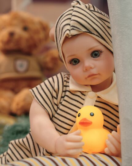 Reborn panenka Bonnie s realistickou silikonovou kůží, oblečená v pruhovaném oblečení, držící žlutou gumu.