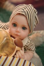 Znovuzrozená panenka s realistickou silikonovou kůží, modrýma očima a detailními rysy, oblečená v pruhované látce.