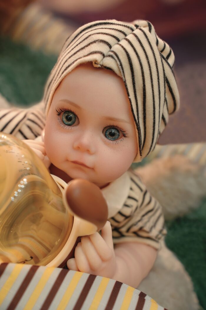 Znovuzrozená panenka s realistickou silikonovou kůží, modrýma očima a detailními rysy, oblečená v pruhované látce.