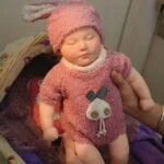 Reborn doll in pink plush outfit with bunny hat, realistic silicone baby for collectors and children.
