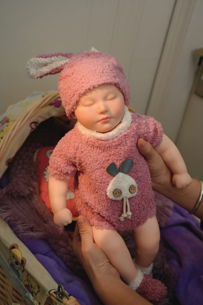 Reborn doll in pink plush outfit with bunny hat, realistic silicone baby for collectors and children.