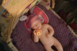 Reborn doll Bonnie, made of silicone, with realistic features, lying on a purple blanket in a cozy s.