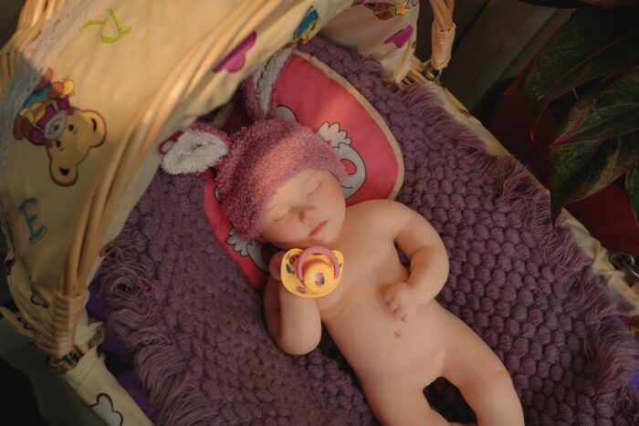 Reborn doll Bonnie, made of silicone, with realistic features, lying on a purple blanket in a cozy s.