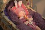 Realistic silicone reborn baby doll with bunny hat in a basket.