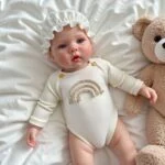 Realistic baby silicone reborn doll wearing a rainbow-themed outfit with teddy bear accessory.