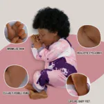 Realistična tamnoputa lutka beba s ukorijenjenom kosom, u pozi za spavanje i detaljnim crtama lica.