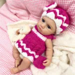 Silikonová panenka Reborn v růžovém pleteném oblečení s čepicí, realistická a ohebná pro sběratele.