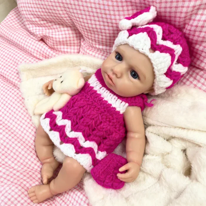 Silikonová panenka Reborn v růžovém pleteném oblečení s čepicí, realistická a ohebná pro sběratele.