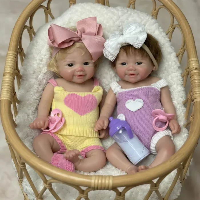 Reālistiskas silikona dvīņu lelles ar sakņotiem matiem, ģērbtas krāsainos tērpos, mājīgā pītā bundžā.