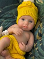 Poupée reborn en silicone, bébé portant un chapeau et une couche jaunes, présentant des traits réalistes et une peau douce.