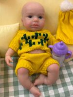 Poupée reborn réaliste en silicone, vêtue de vêtements jaunes et tenant un biberon violet.