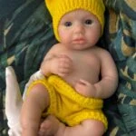 Poupée bébé reborn en silicone aux traits réalistes, vêtue d'un bonnet et d'un short jaunes en tricot, parfaite pour...
