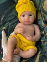 Poupée bébé reborn en silicone aux traits réalistes, vêtue d'un bonnet et d'un short jaunes en tricot, parfaite pour...