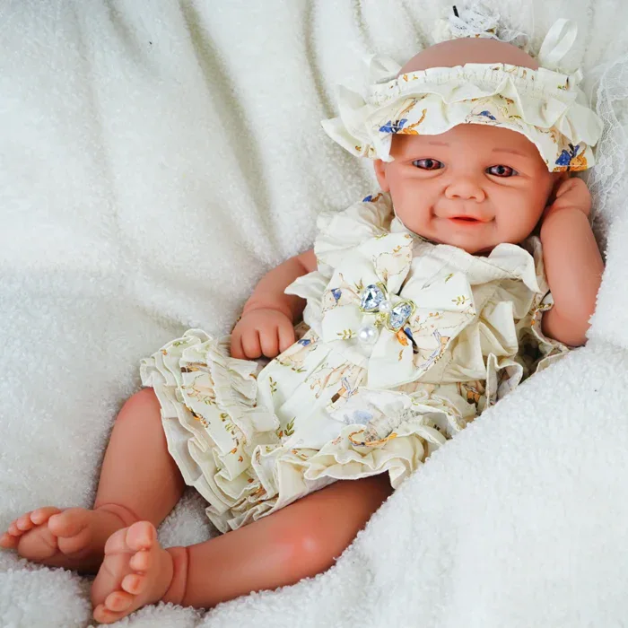 Reborn baby doll with detailed features, dressed in a ruffled cream outfit and matching hat, lying o.