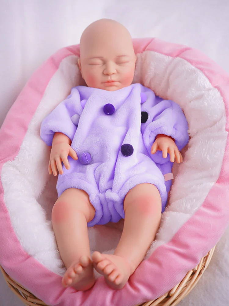 Atgimusi lėlė, gulinti rožiniame krepšyje, aprengta violetiniu drabužiu, tikroviškų bruožų, švelni ir švelni.