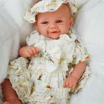 Realistic baby reborn doll dressed in a detailed cream outfit with ruffles and a matching hat.