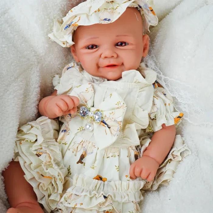 Realistic baby reborn doll dressed in a detailed cream outfit with ruffles and a matching hat.