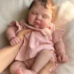 Realistic Baby Reborn doll sleeping, soft pink clothing, lifelike features.