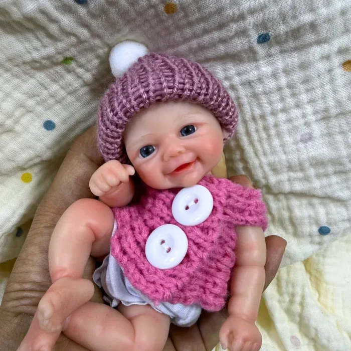 Adorável mini boneca reborn de silicone com gorro e suéter de tricô rosa.