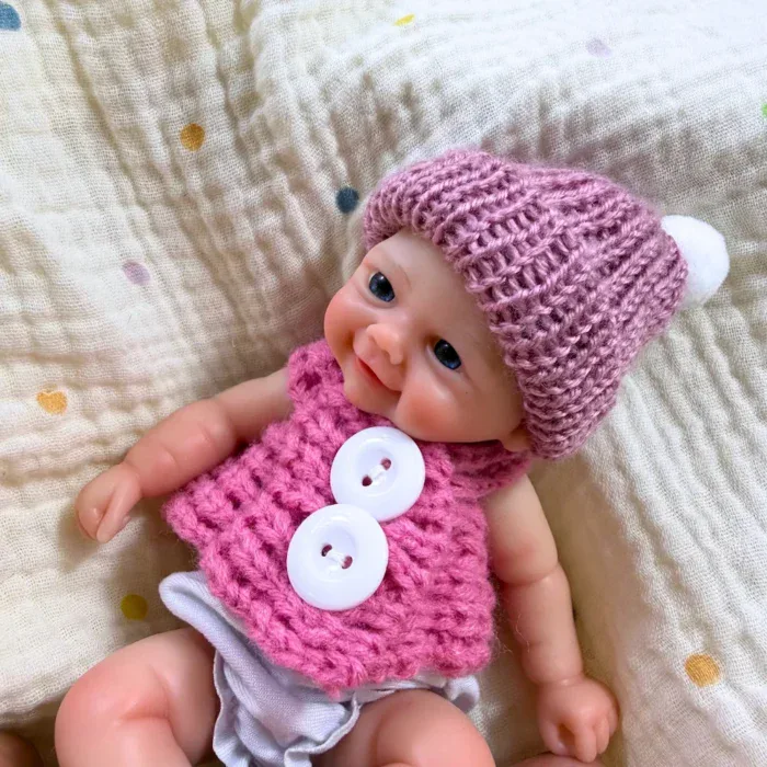 Adorável mini boneca reborn de silicone com roupinha e chapéu rosa.