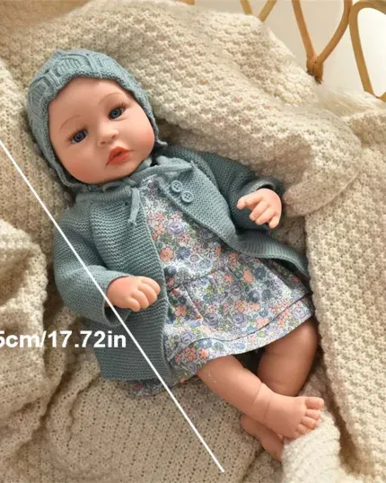 Realistisk babydocka med blå outfit och stickad mössa liggande på filt.