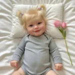 Sød baby pige liggende på pude med lyserøde tulipaner ved siden af hende.