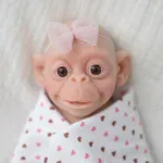 Adorable wide-eyed baby girl silicone reborn doll with pink bow and heart-patterned blanket.