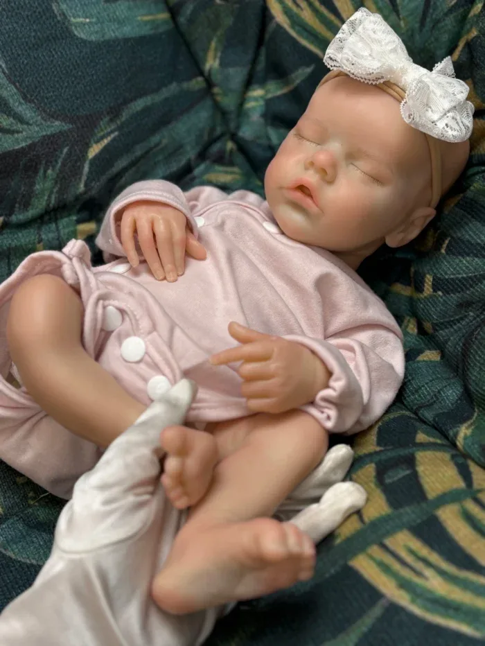 Bebê prematuro realista adormecido, feito de silicone, com faixa de laço na cabeça.