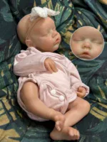 Bebê prematuro realista adormecido, feito de silicone, com faixa na cabeça e roupa rosa.