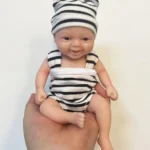 Adorável boneca reborn em miniatura com chapéu e roupa listradas.