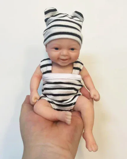 Suloinen miniatyyrikokoinen uudestisyntynyt vauvanukke raidallisessa hatussa ja asussa.