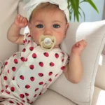 Poupée bébé réaliste aux yeux bleus et avec une tétine, vêtue d'une robe à fraises.