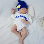 Реалистична бебешка кукла със синя шапка и бяло облекло, спяща спокойно.