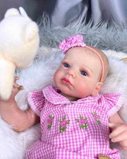 Realistische reborn babypop van een meisje met blauwe ogen, een roze jurk en een haarband.