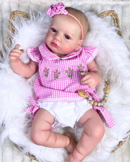 Realistische babypop van een meisje met een roze jurkje en haarband, liggend op een zachte witte deken.