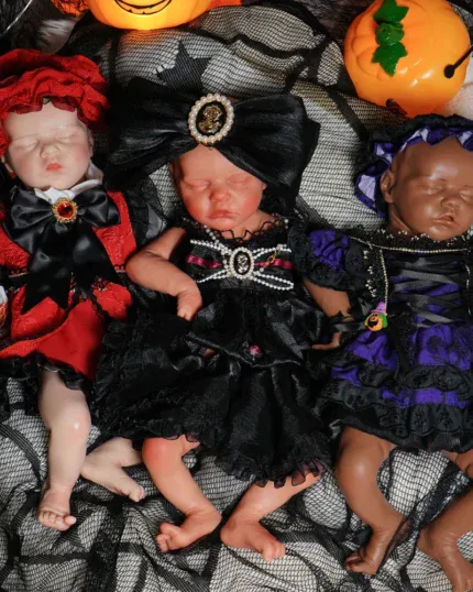 Three Halloween-themed reborn baby dolls in costumes on black fabric.