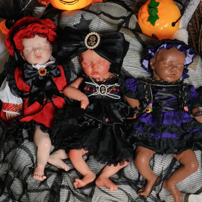 Trois poupées reborn déguisées sur le thème d'Halloween, sur un tissu noir.