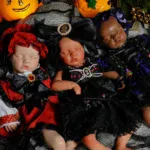 Trois poupées reborn déguisées pour Halloween, avec des citrouilles et des décorations.