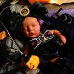 Poupée reborn réaliste sur le thème d'Halloween, avec robe noire et accessoire citrouille.