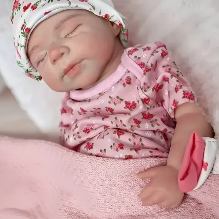 Prim-plan al unei păpuși renăscute care doarme, cu ținută florală și pălărie.