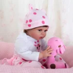 Niedliches Babymädchen mit rosa gepunktetem Hut spielt mit einem rosa Giraffen-Plüschtier.