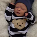 Nahaufnahme einer realistisch wirkenden Babypuppe mit gestreiftem Outfit und Bärenaufnäher.