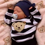Realistische Babypuppe mit Schnuller in gestreifter Kleidung und marineblauem Hut.