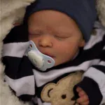 Nahaufnahme einer schlafenden Reborn-Babypuppe (Junge) mit Schnuller und marineblauer Mütze.