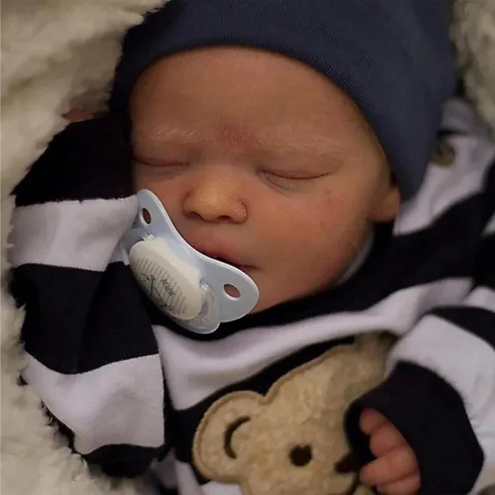 Nahaufnahme einer schlafenden Reborn-Babypuppe (Junge) mit Schnuller und marineblauer Mütze.