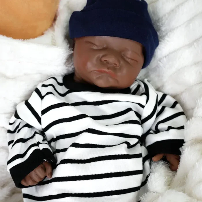 Poupée reborn réaliste de petit garçon noir avec chapeau bleu marine et chemise à rayures.