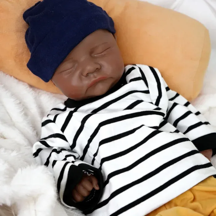 Poupée reborn réaliste de bébé garçon noir de Zion, avec chemise rayée et chapeau bleu marine.
