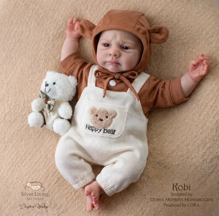 Realistic baby doll with brown bear hoodie and plush toy on beige background.